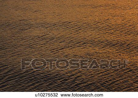 Stock Image - Rippled water reflecting golden light. Fotosearch