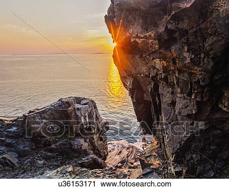 Stock Image - Rock formations by sea at sunrise. Fotosearch