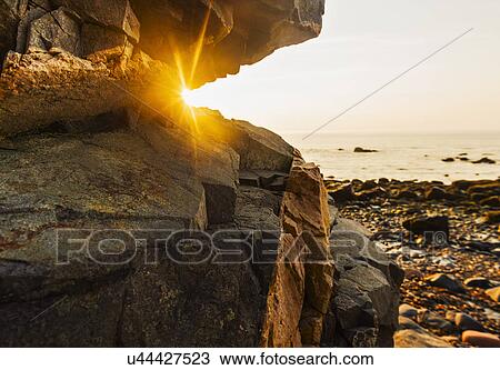 Stock Image - Rock formations on beach and sea at sunrise. Fotosearch