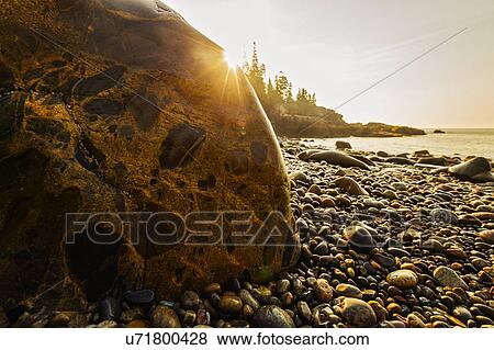 Stock Photo - Rocks and pebbles on beach at sunrise. Fotosearch