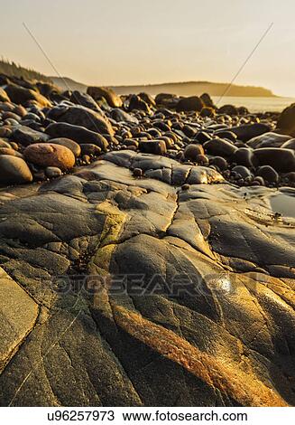 Stock Image - Rocks on beach at sunrise. Fotosearch