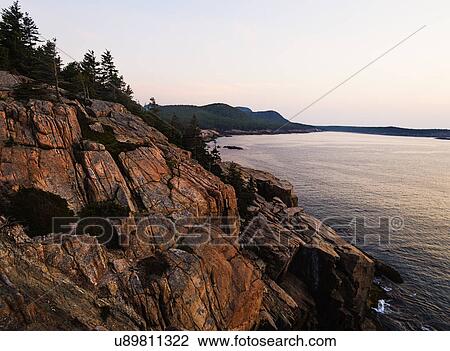 Stock Image - Rocky cliff by sea at sunrise. Fotosearch