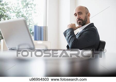 Serious businessman sitting at desk in office View Large Photo Image Stock Image - Serious businessman sitting at desk in office. Fotosearch
