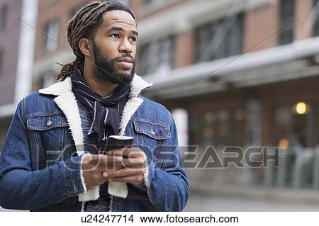 Serious man with dreadlocks holding smart phone in street View Large Photo Image Picture - Serious man with dreadlocks holding smart phone in street. Fotosearch