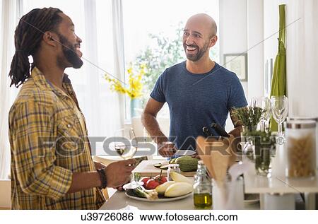 Stock Photograph - Smiley homosexual couple drinking wine in kitchen. Fotosearch