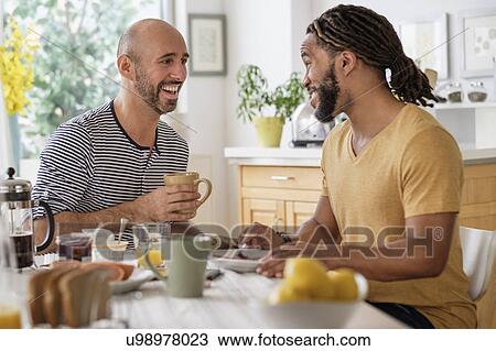 Stock Image - Smiley homosexual couple having breakfast in kitchen. Fotosearch