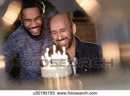 Stock Image - Smiley homosexual couple looking at birthday cake. Fotosearch