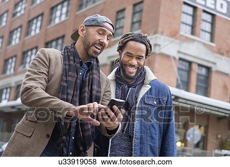 Smiley homosexual couple looking at smart phone in street View Large Photo Image Stock Photo - Smiley homosexual couple looking at smart phone in street. Fotosearch