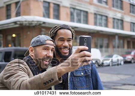 Smiley homosexual couple taking selfie with smart phone in street View Large Photo Image Stock Image - Smiley homosexual couple taking selfie with smart phone in street. Fotosearch