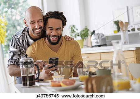 Smiley homosexual couple using smart phone at dinner table View Large Photo Image Stock Photography - Smiley homosexual couple using smart phone at dinner table. Fotosearch