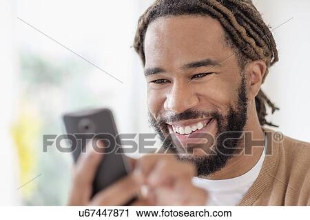 Stock Image - Smiley young man with dreadlocks using smart phone. Fotosearch