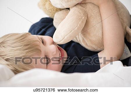 Stock Photograph - Smiling boy (2-3) with toy lying down on bed. Fotosearch