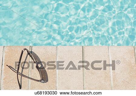 Stock Image - Sunglasses on brick ledge by pool. Fotosearch