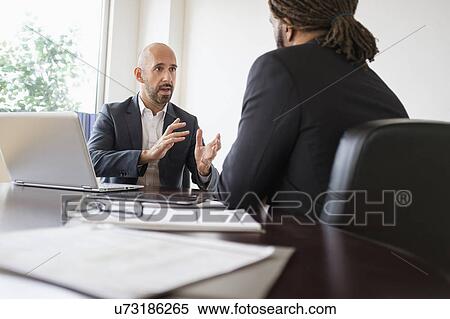 Stock Photography - Two businessmen having discussion at desk in office. Fotosearch