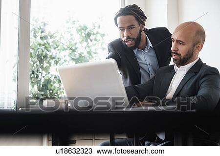 Two businessmen working with laptop by desk in office View Large Photo Image Stock Image - Two businessmen working with laptop by desk in office. Fotosearch
