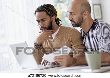 Stock Image - Two men working with laptop at table at home. Fotosearch