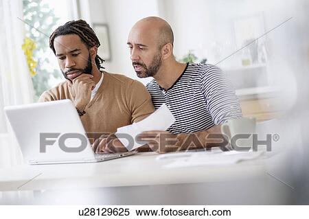 Two men working with laptop at table at home View Large Photo Image Stock Photography - Two men working with laptop at table at home. Fotosearch