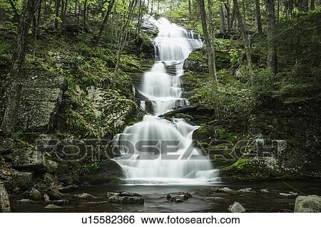 Stock Photograph - Waterfall falling into river in middle of forest. Fotosearch