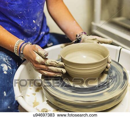 Stock Image - Woman shaping clay bowl on pottery wheel. Fotosearch