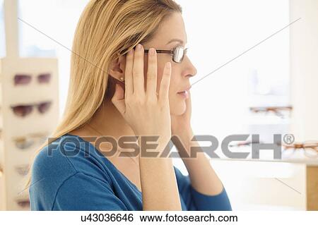 Stock Photograph - Woman trying on eyeglasses in store. Fotosearch