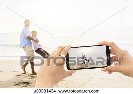 Picture - Young woman photographing father with son (12-13) on beach. Fotosearch
