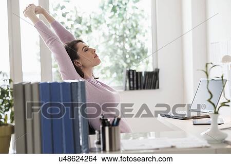 Picture - Young woman stretching by desk. Fotosearch