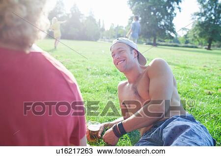 Stock Image - Adult friends relaxing at sunset park party. Fotosearch