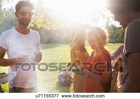 Stock Photo - Adults friends eating and drinking at sunset party in park. Fotosearch