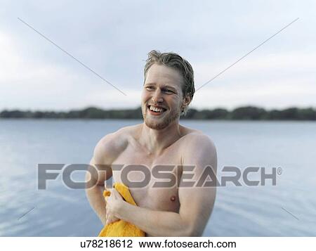 Stock Image - Bare chested young man drying off with towel, looking away smiling, Copenhagen, Denmark. Fotosearch