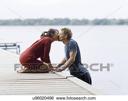 Stock Photograph - Couple on pier face to face holding hands kissing, Copenhagen, Denmark. Fotosearch