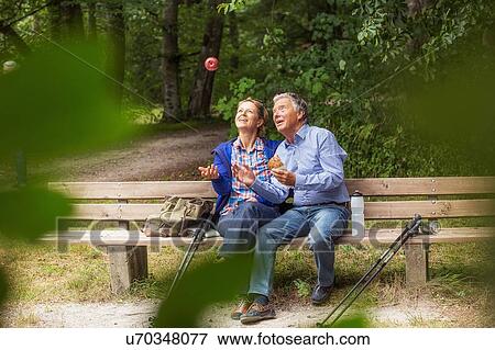 Stock Photo - Couple sitting on bench in forest, woman throwing apple in air. Fotosearch