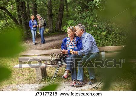 Stock Photo - Couple sitting on bench in forest, looking at view. Fotosearch