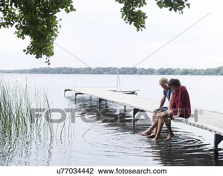 Couple sitting on pier side by side dipping toes in water, Copenhagen, Denmark View Large Photo Image Stock Image - Couple sitting on pier side by side dipping toes in water, Copenhagen, Denmark. Fotosearch