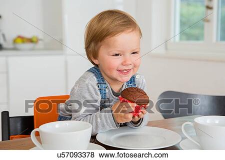 Cute female toddler holding cupcake at kitchen table View Large Photo Image Stock Photo - Cute female toddler holding cupcake at kitchen table. Fotosearch
