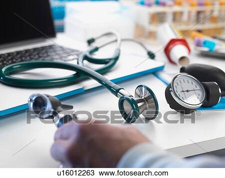 Doctor picking up auriscope with stethoscope and blood pressure gauge from desk View Large Photo Image Stock Image - Doctor picking up auriscope with stethoscope and blood pressure gauge from desk. Fotosearch