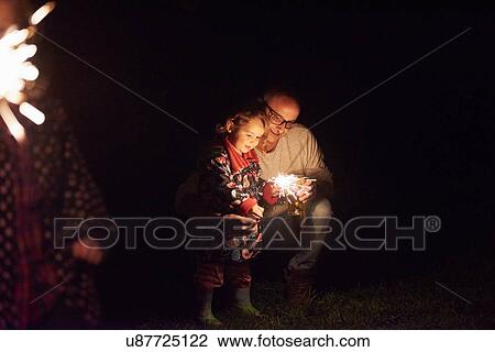 Stock Image - Father crouching next to daughter holding sparkler. Fotosearch