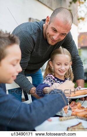 Father helping children at garden barbecue table View Large Photo Image Stock Image - Father helping children at garden barbecue table. Fotosearch