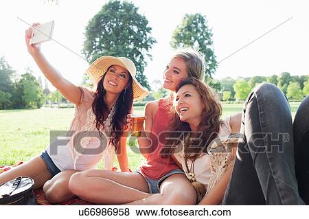 Stock Photo - Female friends taking smartphone selfie at park party. Fotosearch