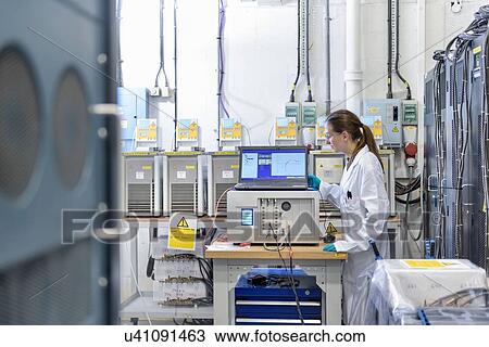 Stock Image - Female scientist with battery aging test equipment in battery research facility. Fotosearch