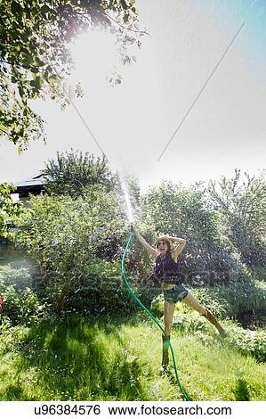 Front view of mature woman in garden standing on one leg squirting water into air with hosepipe View Large Photo Image Stock Photograph - Front view of mature woman in garden standing on one leg squirting water into air with hosepipe. Fotosearch