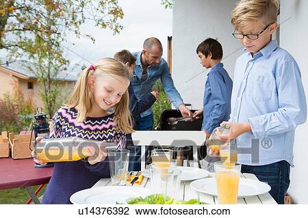 Girl and brother pouring juice at garden barbecue table View Large Photo Image Stock Image - Girl and brother pouring juice at garden barbecue table. Fotosearch