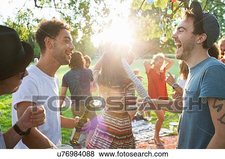 Stock Photo - Group of adult friends chatting at party in park at sunset. Fotosearch