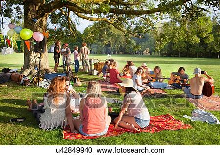 Group of friends listening to music under park tree at sunset party View Large Photo Image Stock Image - Group of friends listening to music under park tree at sunset party. Fotosearch