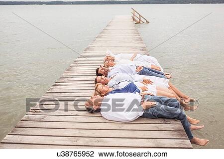 Stock Image - Group of friends lying in a row, on pier. Fotosearch