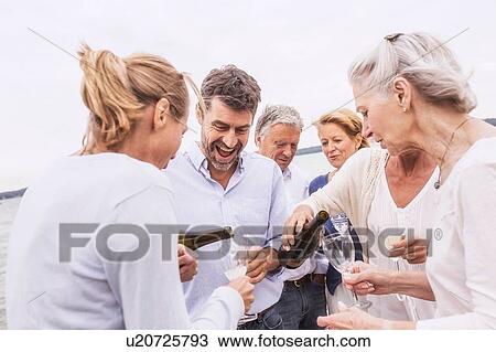 Stock Image - Group of friends pouring wine into wine glasses. Fotosearch