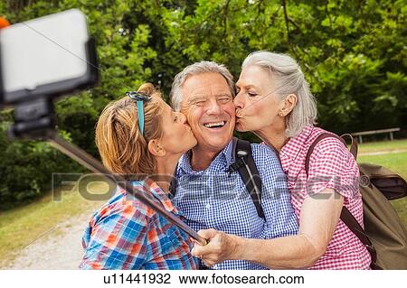 Group of friends taking self portrait, using selfie stick and smartphone, women kissing man on cheek View Large Photo Image Stock Image - Group of friends taking self portrait, using selfie stick and smartphone, women kissing man on cheek. Fotosearch