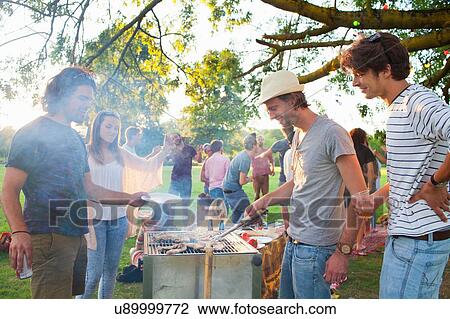 Happy adult friends barbecuing at sunset party in park View Large Photo Image Stock Image - Happy adult friends barbecuing at sunset party in park. Fotosearch