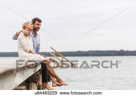 Stock Photo - Mature couple sitting on edge of pier, relaxing. Fotosearch