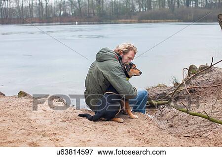 Stock Photo - Mature man hugging dog on riverbank. Fotosearch