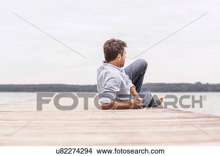Picture - Mature man relaxing on pier, rear view. Fotosearch